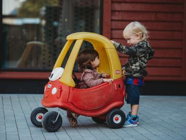Barn kører med et andet barn i en rød og gul bil